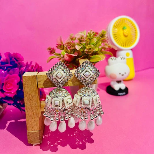Decorative earrings on a stand with a pink background and decorative items.