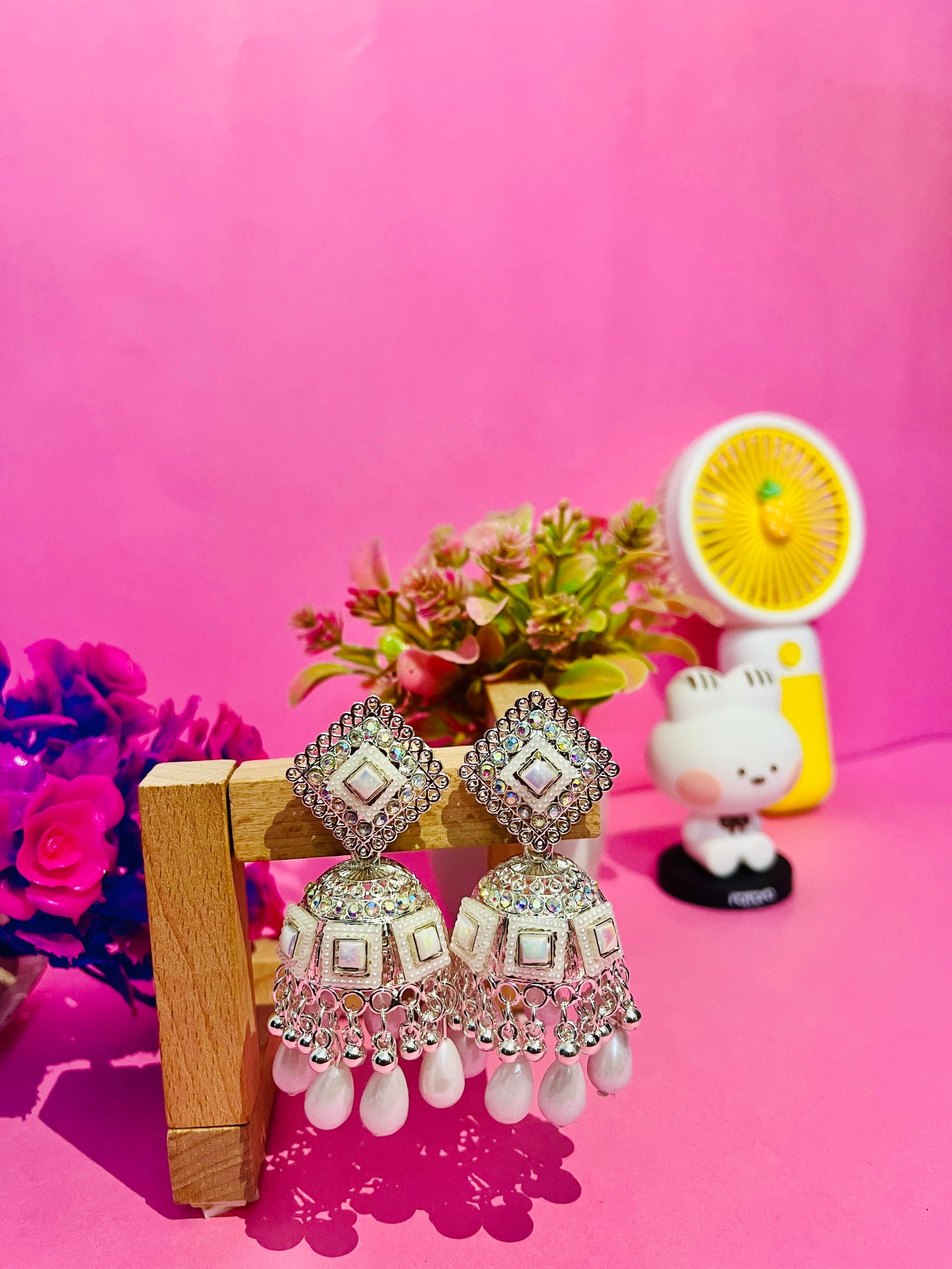 Decorative earrings on a stand with a pink background and decorative items.